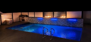 A swimming pool with a stone wall and built-in fire feature. - Poolside Oasis (West Kelowna)