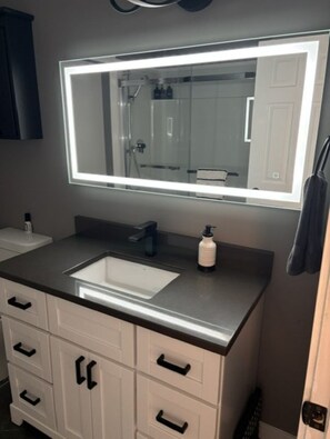 Une salle de bain avec un grand miroir, un lavabo et un meuble-lavabo doté de tiroirs.