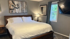 Un dormitorio con cama, mesitas de noche, lámpara, televisor y obras de arte en las paredes.