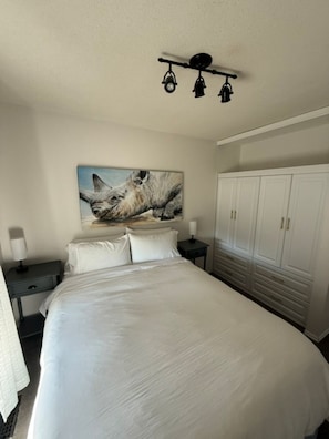 A bedroom with a large bed, a painting of a cat, a wardrobe, and a ceiling light fixture. - Poolside Oasis (West Kelowna)
