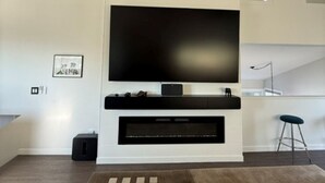 Una sala de estar moderna con un televisor de pantalla plana grande, un sistema de sonido integrado y un piso de madera oscura.