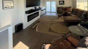 Amplia sala de estar con una gran televisión de pantalla plana, ventilador de techo, sofá modular y chimenea.