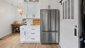 Una cocina con armarios blancos, un refrigerador de acero inoxidable y una encimera de madera.