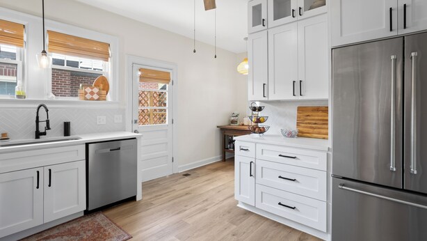 Una cocina moderna con armarios blancos, electrodomésticos de acero inoxidable y un ventilador de techo de madera.