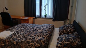 Ett sovrum med en stor säng, ett skrivbord, en stol och ett fönster med gardiner.