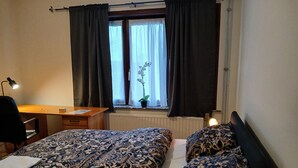 Ett sovrum med två sängar, ett skrivbord, en stol, ett element och ett fönster med gardiner.