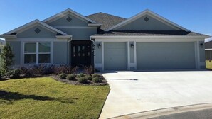 A two-story house with a garage, a front door, and a driveway. - GORGEOUS 3-bedroom house with NEW golf cart in The Villages! Perfect location! (The Villages)