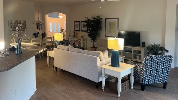 A living room with a sofa, a patterned armchair, a TV, and a ceiling fan. - GORGEOUS 3-bedroom house with NEW golf cart in The Villages! Perfect location! (The Villages)