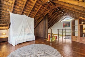 Une pièce aux hauts plafonds, avec un plafond en bois, un lit à baldaquin blanc, un tapis tissé et une vue sur l’extérieur grâce à une porte vitrée.