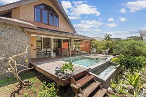 A house with a stone exterior, a wooden deck, a swimming pool, and a covered patio area.