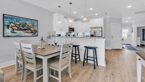 Een moderne keuken met witte kasten, een houten eettafel en barstoelen.