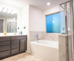 Ein modernes Badezimmer mit Badewanne, dunklen Schränken, einem großen Spiegel und einem Fenster mit blauer Tönung.