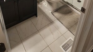 Un baño moderno con ducha de vidrio, inodoro blanco y tocador oscuro con espejo.