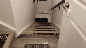 Una escalera estrecha con un rellano alfombrado, una puerta al final y una barandilla a la izquierda.