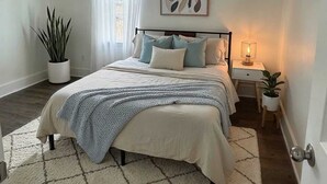 A bedroom with a bed, bedside tables, a potted plant, and a window with curtains. - Austin Living at Picnic Dr , Modern, Private & Bright (Round Rock)
