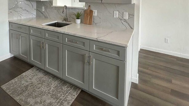 A modern kitchen with grey cabinets, a marble countertop, and a wooden cutting board. - Austin Living at Picnic Dr , Modern, Private & Bright (Round Rock)