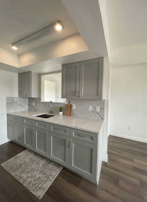 A modern kitchen with grey cabinets, a marble countertop, and a wooden cutting board.