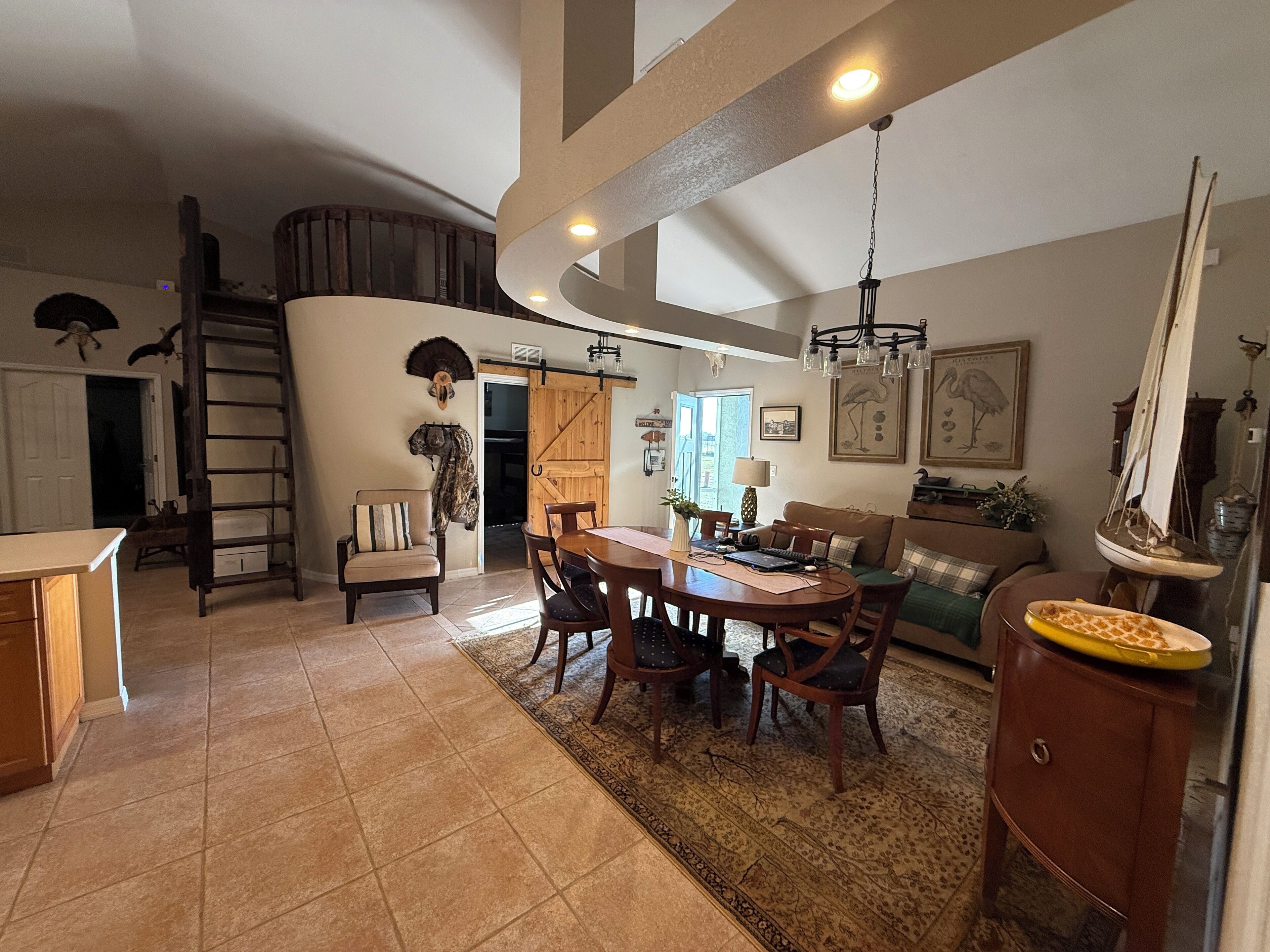 A spacious dining area with a wooden table and chairs, a loft with a ladder, and a large window.