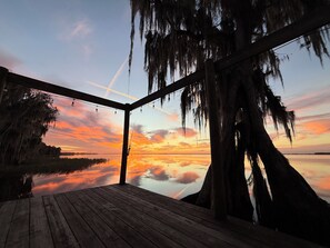 Eine Holzterrasse mit Blick auf einen Sonnenuntergang über ruhigem Wasser, umgeben von Bäumen mit spanischem Moos.