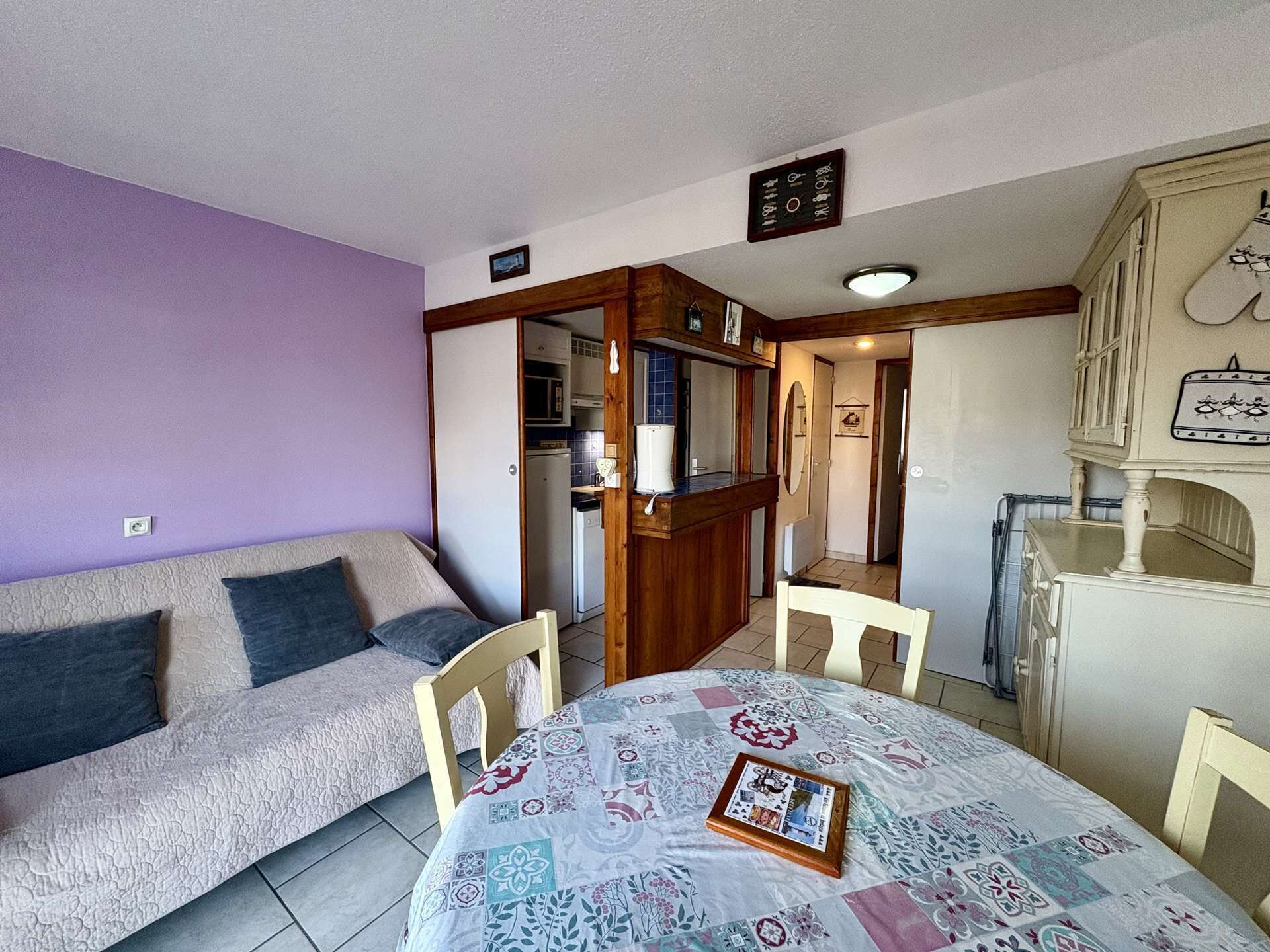Ein gemütliches Zimmer mit einer Couch, einem Esstisch mit einer Steppdecke, einer Küchenzeile und einem kleinen Schrank.