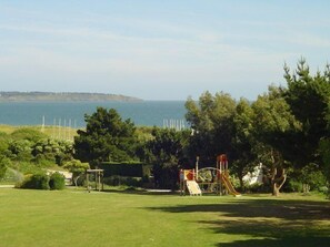 Ein Park mit einem Spielplatz, einer Rasenfläche und Blick auf das Meer.