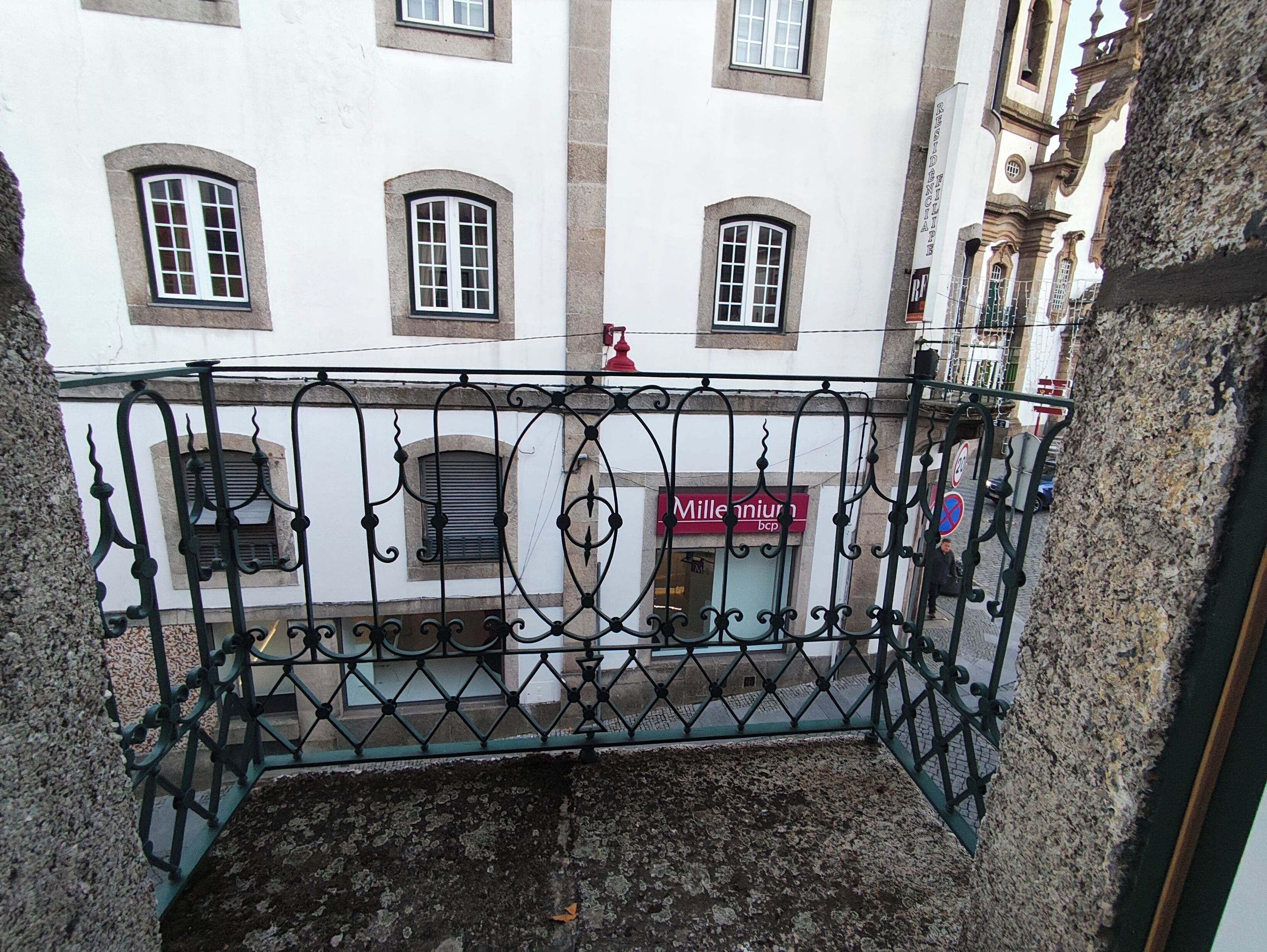 Un balcón con barandillas de hierro forjado, un edificio con ventanas de arco y una tienda con un letrero rojo.
