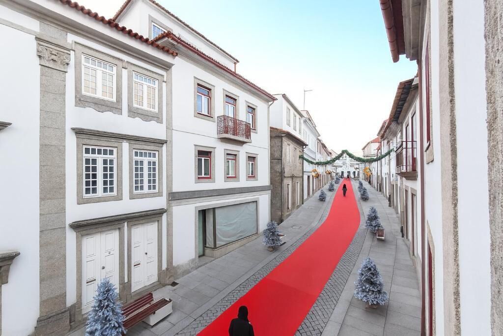 A narrow street lined with white buildings, a red carpet, and small Christmas trees.