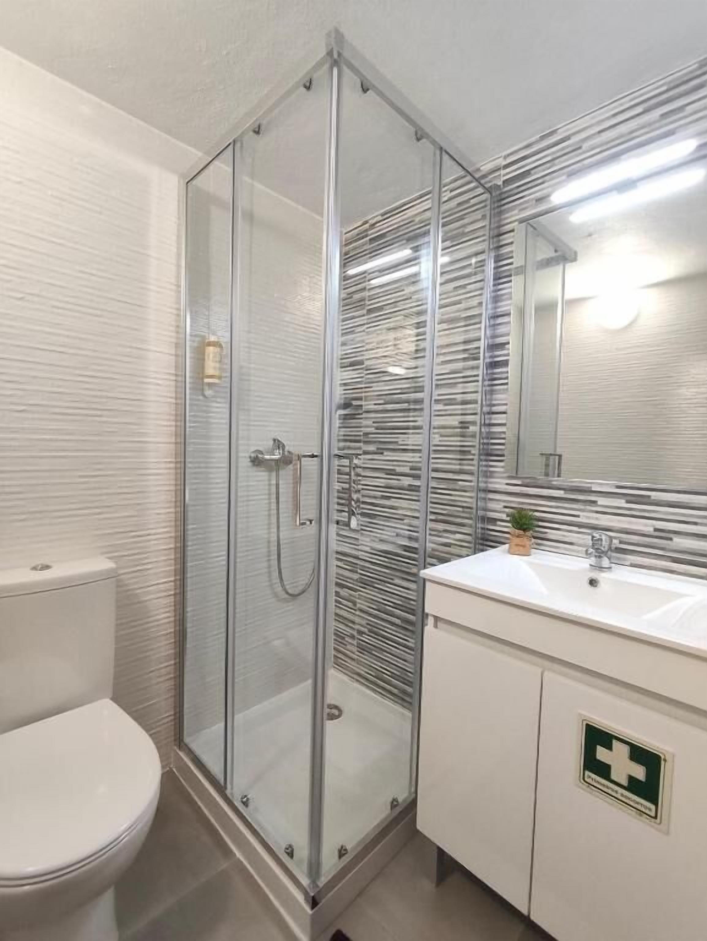 Un baño moderno con ducha de vidrio, inodoro blanco y lavamanos con espejo.