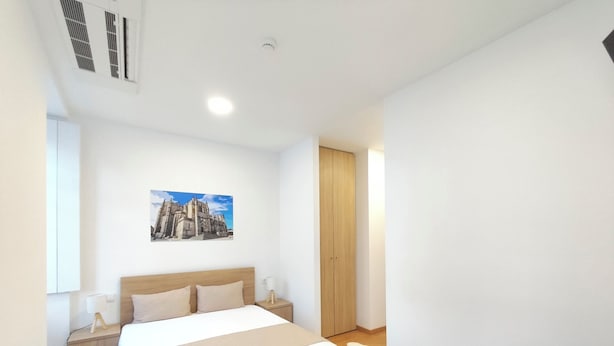 A modern bedroom with a large bed, a nightstand, a wooden wardrobe, and a painting on the wall. - Misericordia Rooms (Guarda)