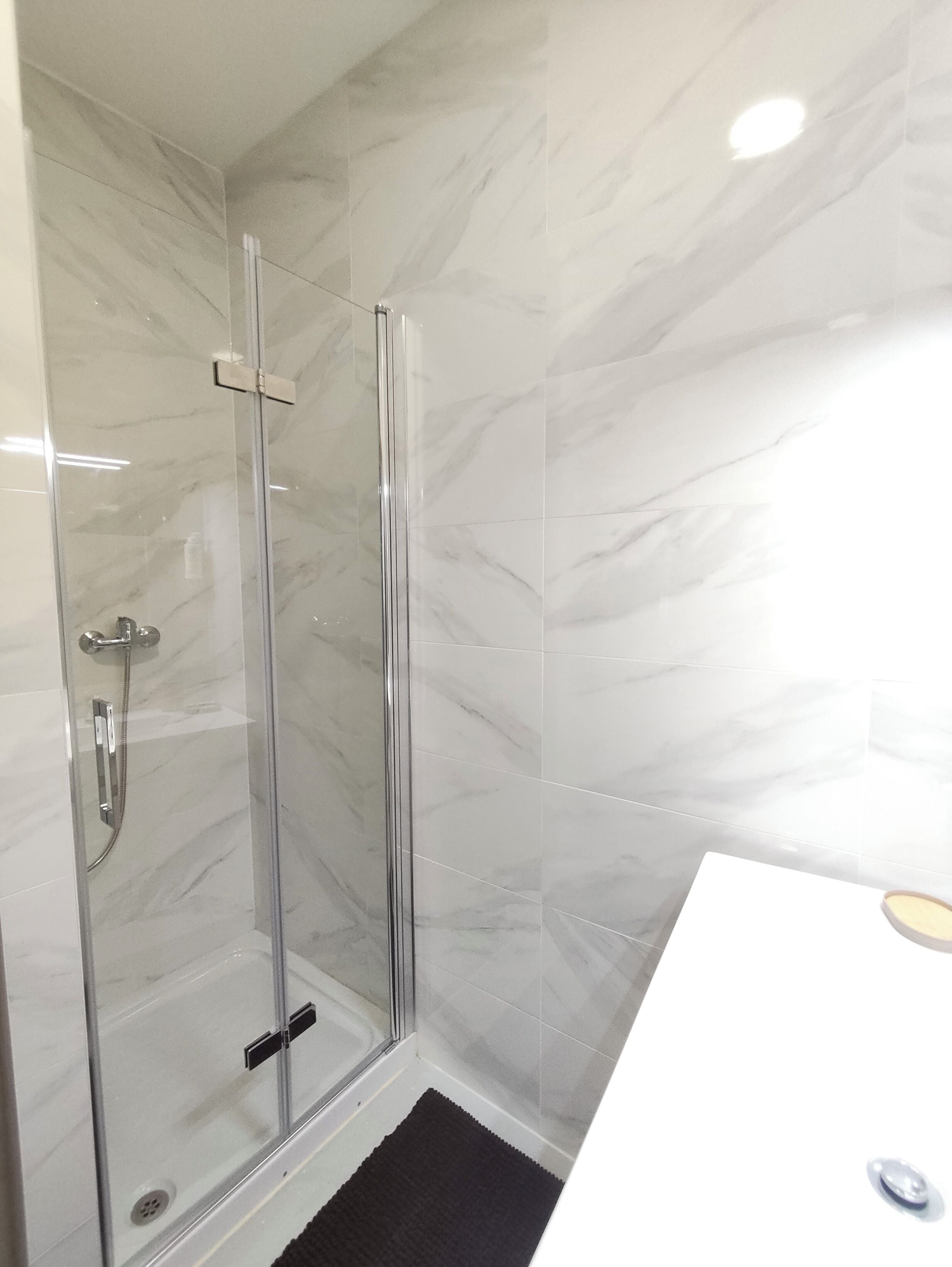 Een moderne badkamer met een douchecabine van glas, witte marmeren tegels en een wit wastafelmeubel met een houten aanrecht.