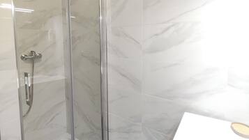 Een moderne badkamer met een douchecabine van glas, witte marmeren tegels en een wit wastafelmeubel met een houten aanrecht.
