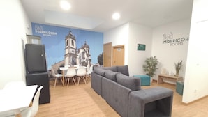 A modern waiting area with a grey sofa, white chairs, a small table, and a mural of a church. - Misericordia Rooms (Guarda)