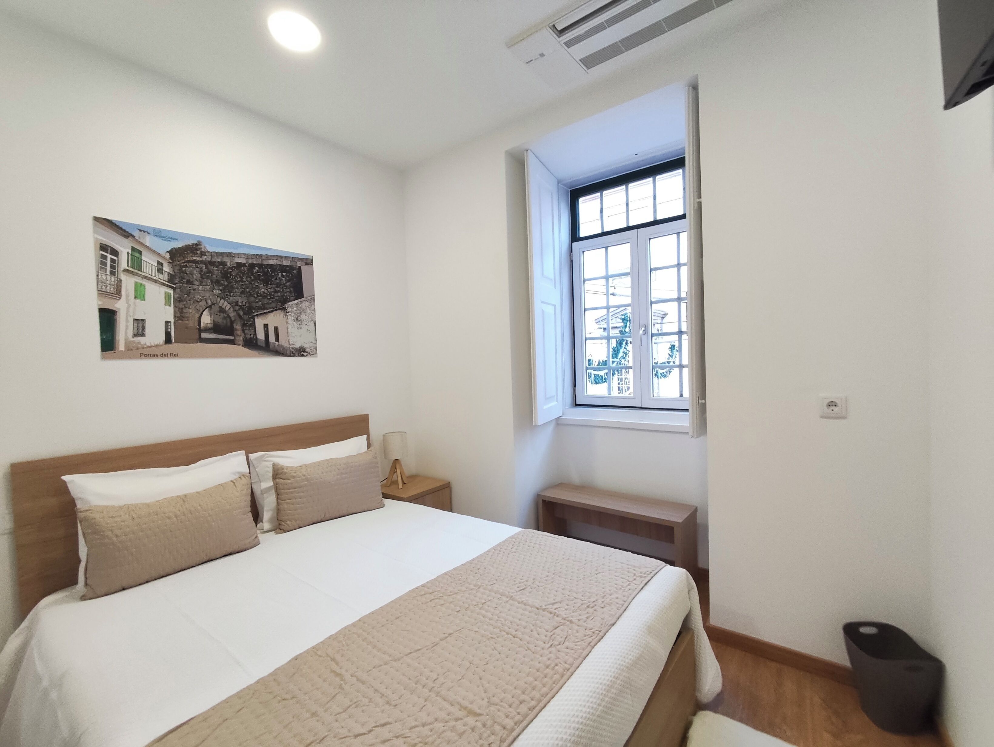 A bedroom with a bed, a nightstand, a window, and a wall-mounted picture.