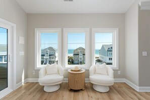 A room with three large windows, a round wooden table, and two white armchairs. - Luxury Beach Retreat, 7BR, Dock, 360° Views (North Topsail Beach)