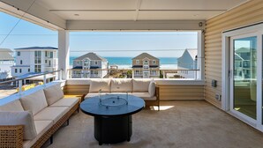 Un balcon avec un canapé, une table ronde et une vue sur l’océan et les maisons de plage.