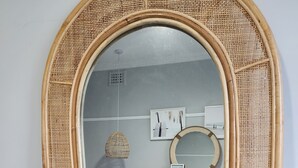 A room with a large mirror framed in woven material, a bed with blue bedding, and a hanging light fixture.
