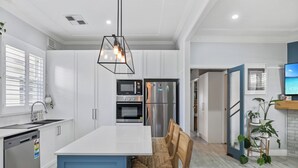 A modern kitchen with a central island, built-in appliances, and a dining area with a wooden chair.