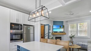 A modern kitchen with built-in appliances, a dining area with a wooden table and chairs, and a TV mounted above a fireplace.