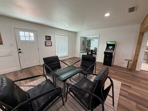 A room with a glass-top table surrounded by four black leather chairs, a white door, a window with blinds, and a vending machine. - Pecan Grove | Spacious South Abilene Stay (Abilene)