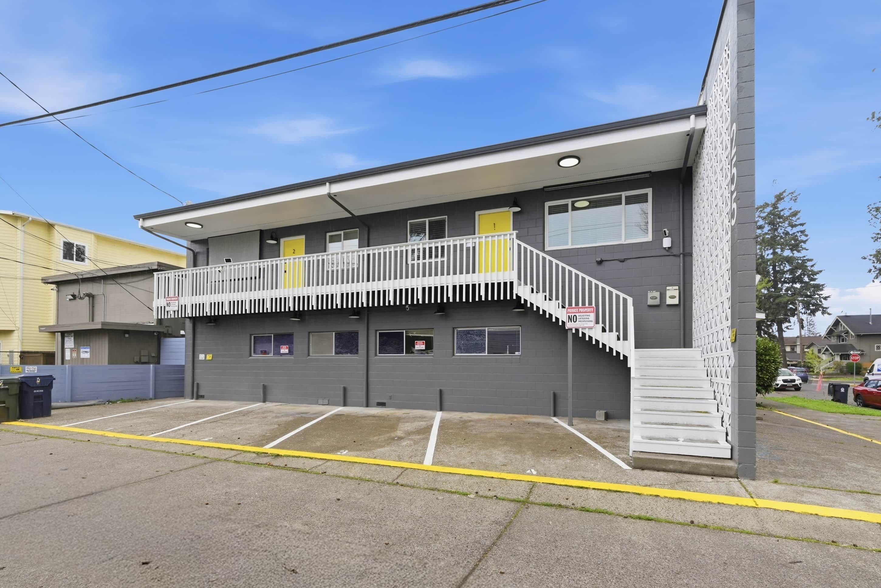 A two-story building with a balcony, a parking lot, and a gated entrance.