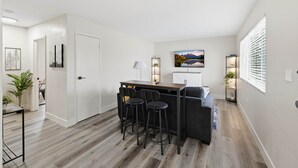 A modern living room with a dark-colored sofa, a small dining area with two stools, and a painting on the wall. - UO•Downtown (1/2 mile)•West University •King Suite (Eugene)