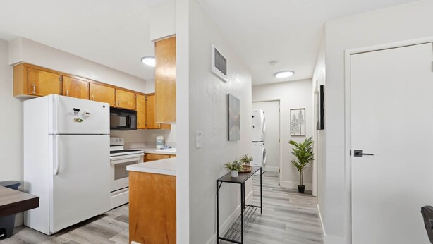 A modern kitchen with wooden cabinets, a white refrigerator, and a microwave. There is a small table with a plant, and a door leading to another room. - UO•Downtown (1/2 mile)•West University•King Suite (Eugene)
