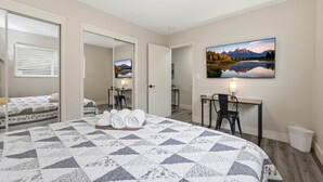 A hotel room with a large bed, a desk, a chair, a mirror, and a painting of a mountain landscape. - UO•Downtown (1/2 mile)•West University•King Suite (Eugene)