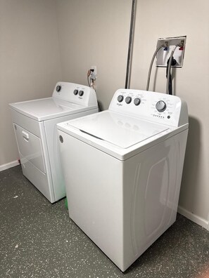Zwei weiße Waschmaschinen mit Frontlader in einem Waschraum mit grau gemustertem Boden und einer Funktionswand mit Warmwasserbereiter.