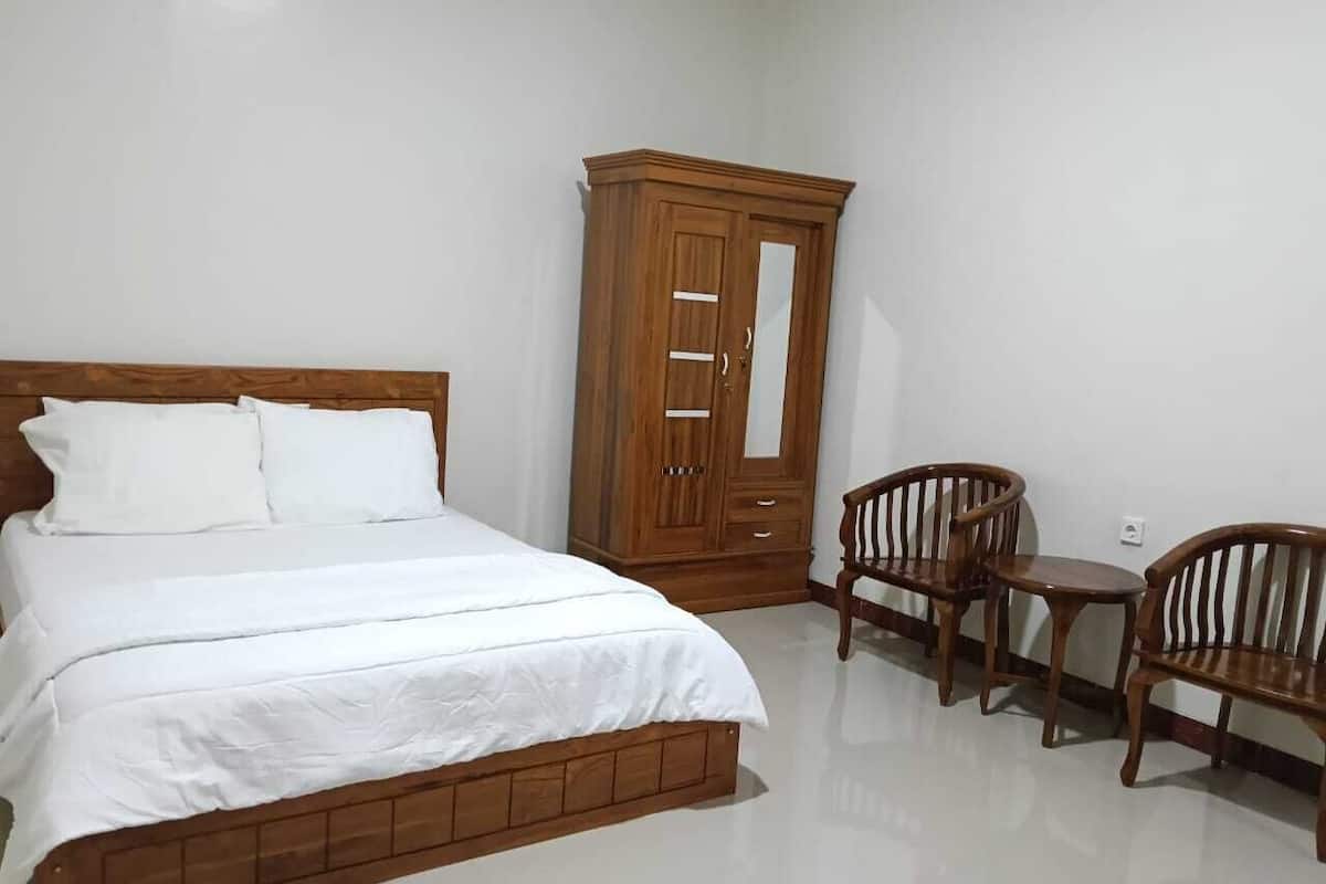 A bedroom with a bed, wooden wardrobe, and two wooden chairs.