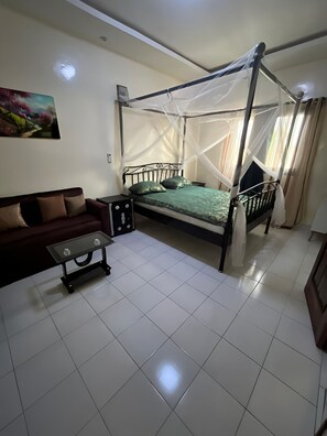 A room with a four-poster bed, a sofa, a small table, and a painting on the wall. - Modern Studio Sacré-Cœur 2 Dakar - 2 Baths, Balcony, AC, WiFi - Secure Residence (Dakar)