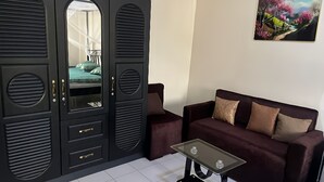 Een kamer met een grote zwarte garderobe, een salontafel met een glazen blad, een donkerbruine bank en een schilderij aan de muur.
