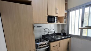 Een moderne keuken met lichte houten kastjes, een roestvrijstalen fornuis, een magnetron en een spoelbak.
