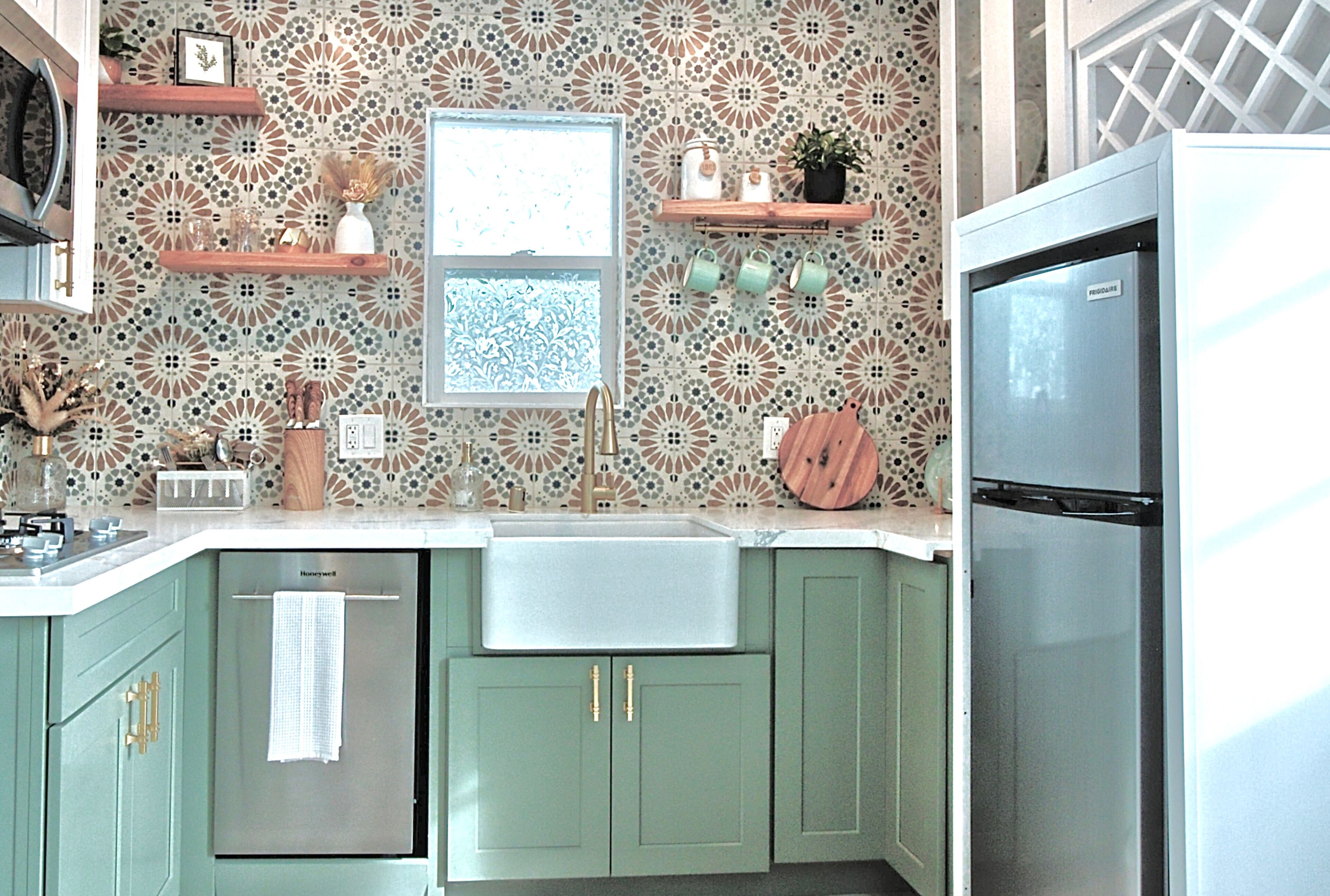 A kitchen with green cabinets, a stainless steel refrigerator, and a patterned backsplash.