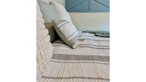 Ein Bett mit einer gestreiften Bettdecke und mehreren Kissen, darunter eines weiß mit Karomuster.